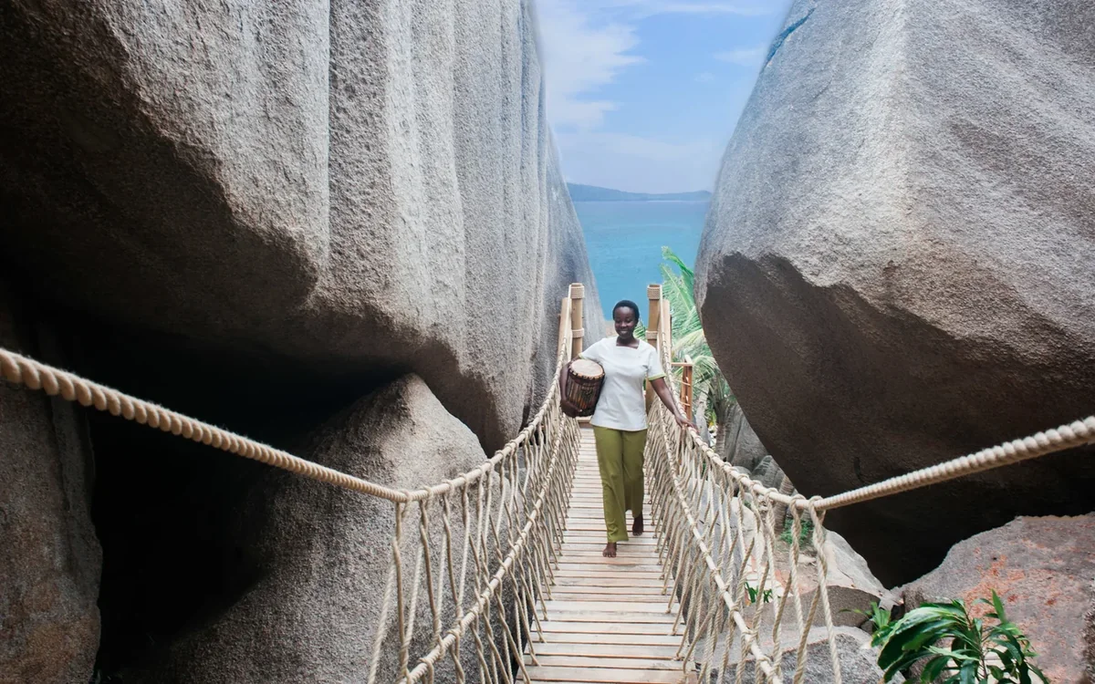 Spa host crossing a rope bridge between granite boulders